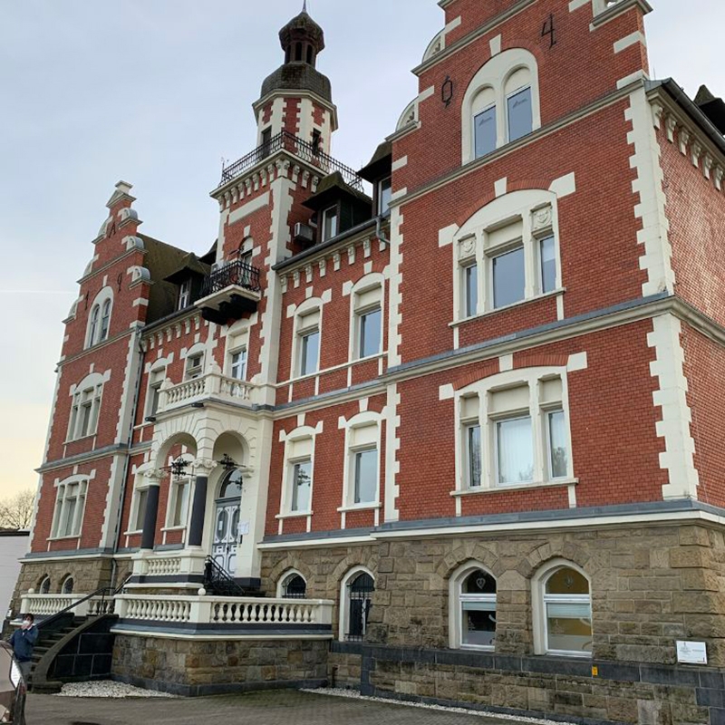 Außenansicht Gebäude der dmt. Physiotherapie-Niederlassung. Altes 3-stöckiges Gebäude mit imposantem Eingangsbereich und roter Backstein-Fassade.