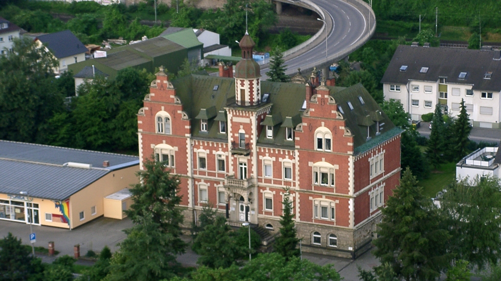 Gebäude der dmt. Physiotherapie-Praxis in Bad Breisig. Altes ehrwürdiges Gebäude mit roter Klinkerfront. Bild ist eine Luftaufnahme.