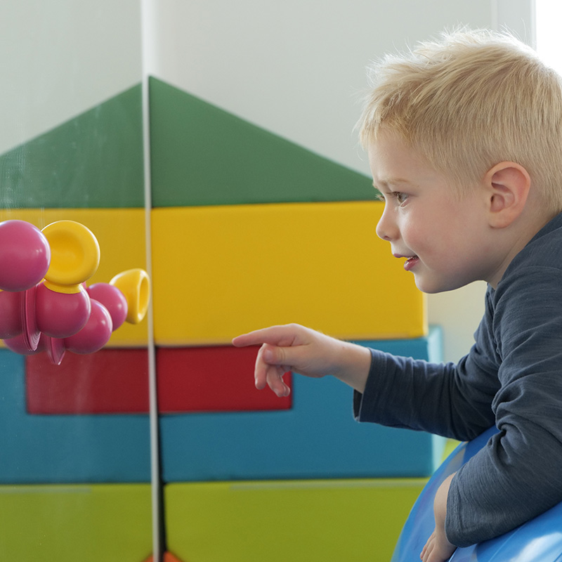 dmt. Kids. Physiotherapie-Übung mit einem Kind im Kindergartenalter vor einem Spiegel im Übungsraum.