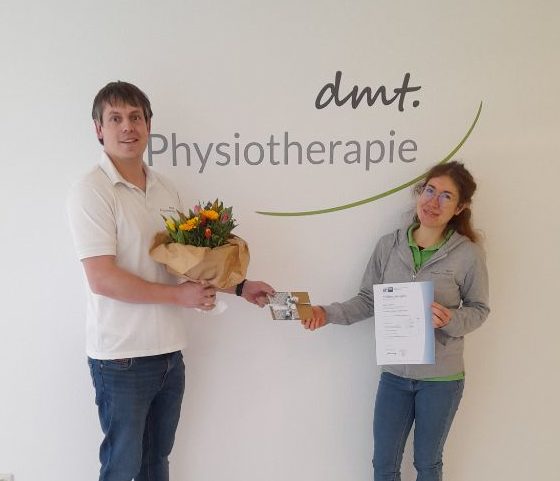 Dennis gratuliert Maren vor dem dmt. Physiotherapie Logo.