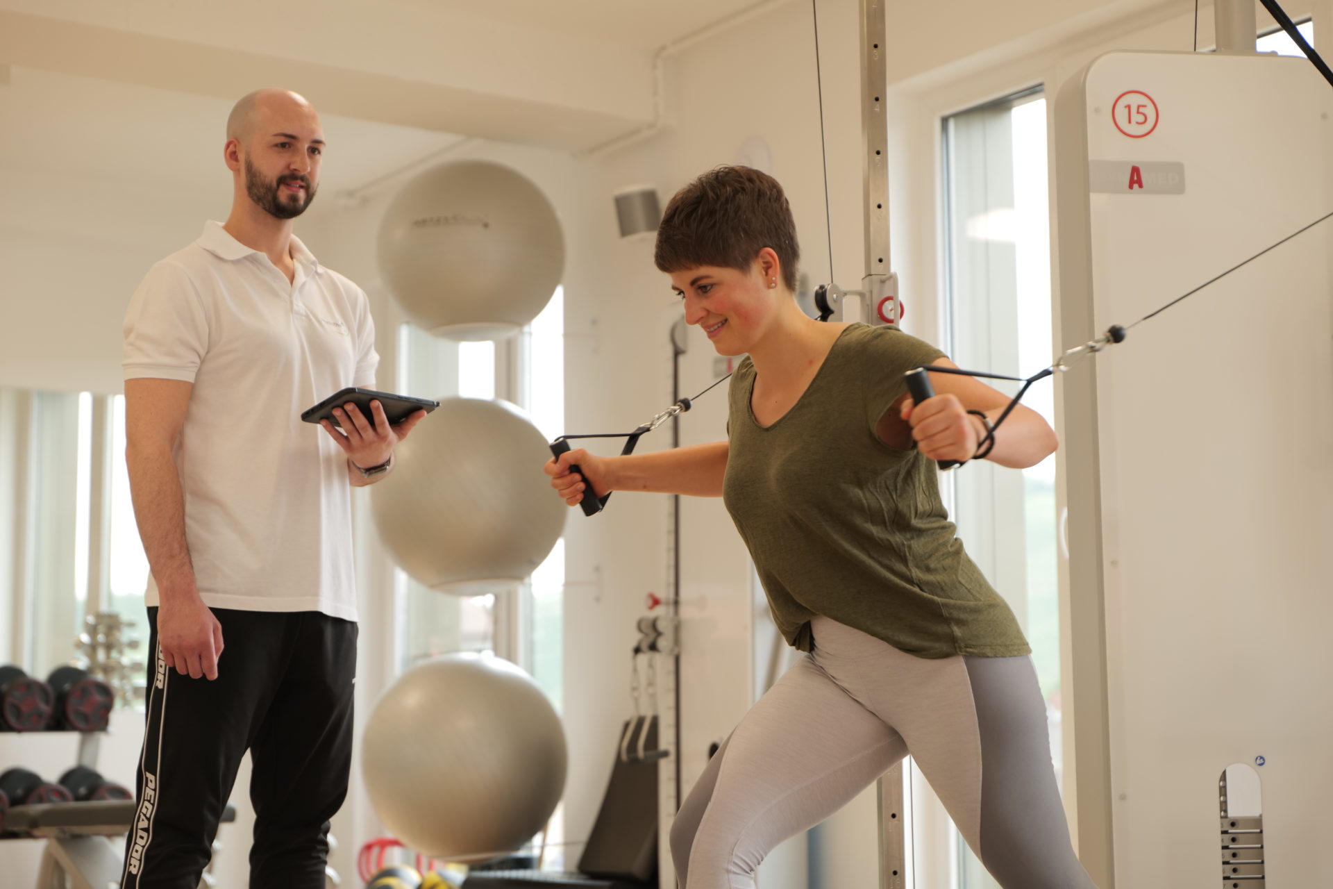 Man sieht Dominik in der Physiotherapiepraxis, wie er eine Patienten am Kabelzug betreut.