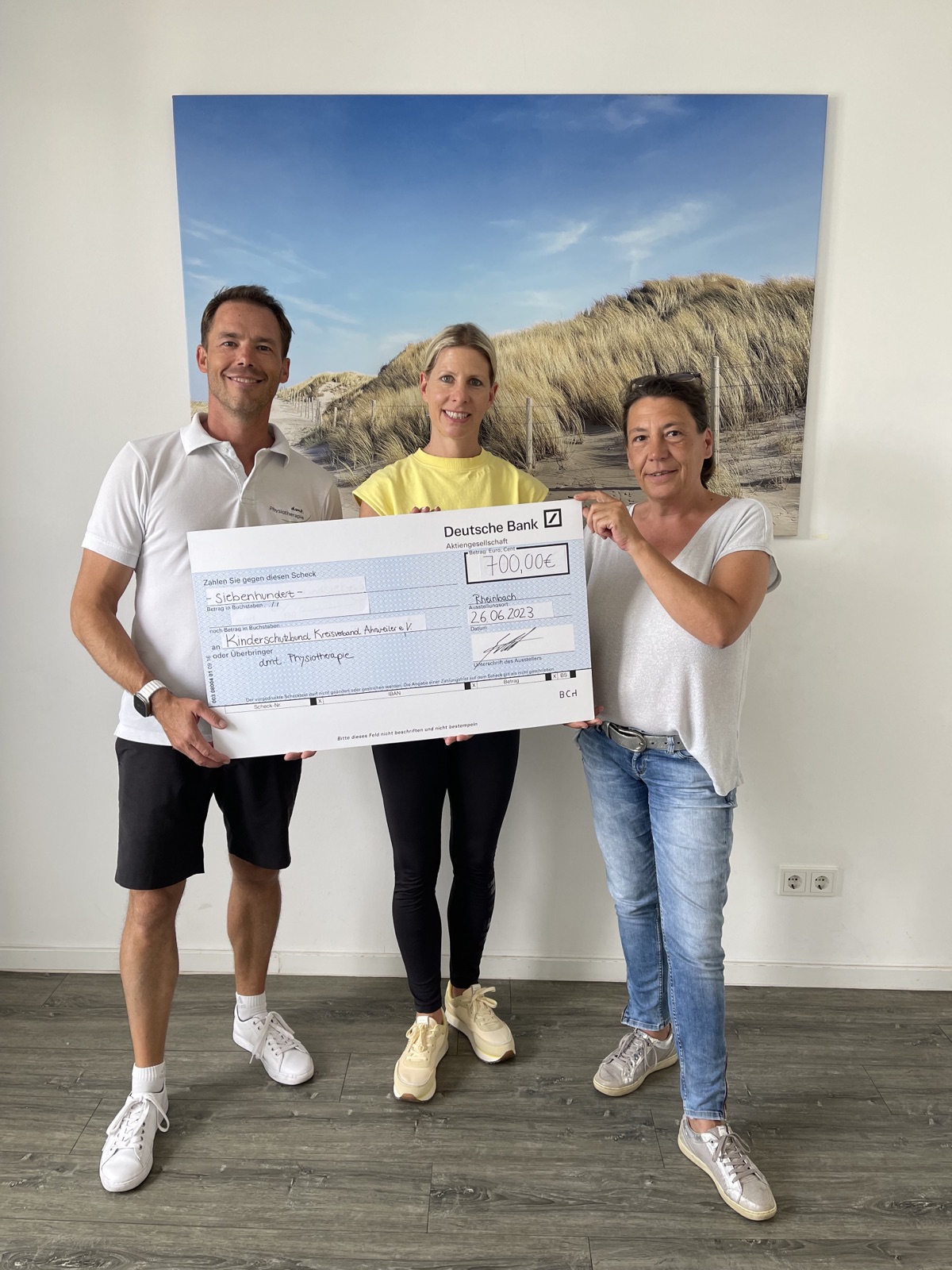 Tino und zwei Vertreterinnen des Kinderschutzbunds Ahrweiler halten einen Spendencheck der dmt. Physiopraxis in den Händen, Höhe 700,00€.