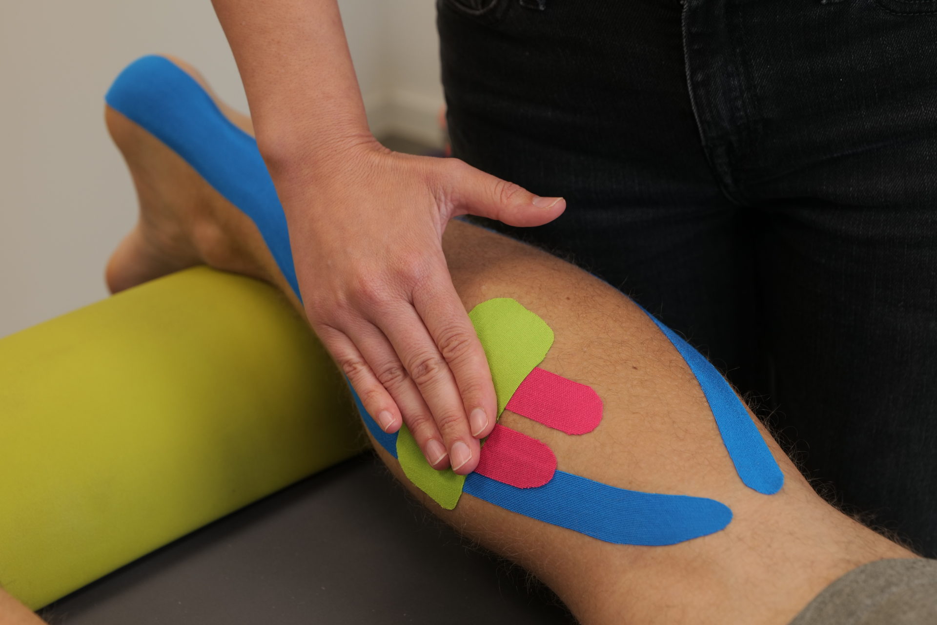 Man sieht einen getapten Unterschenkel. Der Physiotherapeut fixert das Tape mit seinen Händen.