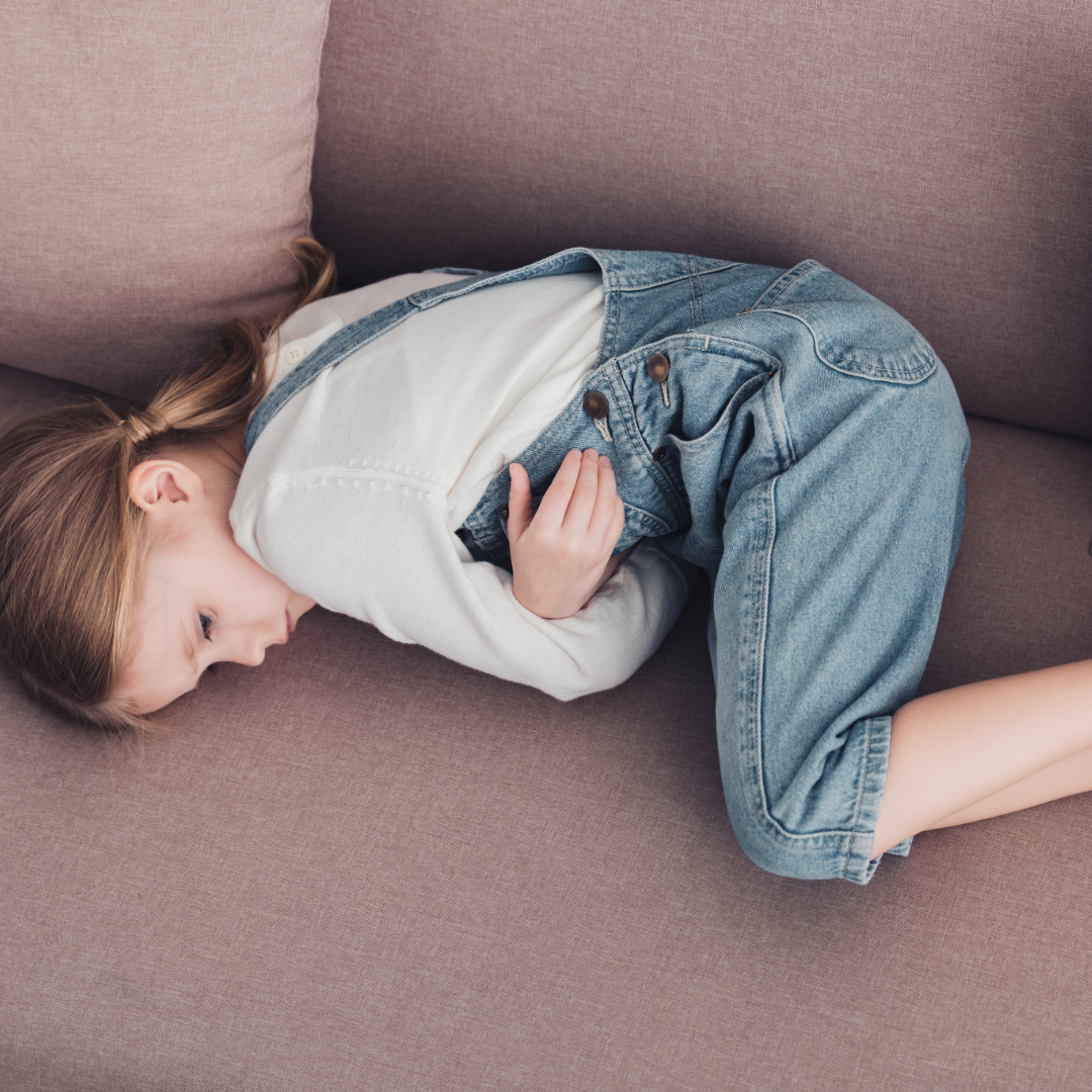 Ein Kind liegt zusammengerollt auf dem Sofa. Ihr geht es nicht gut.