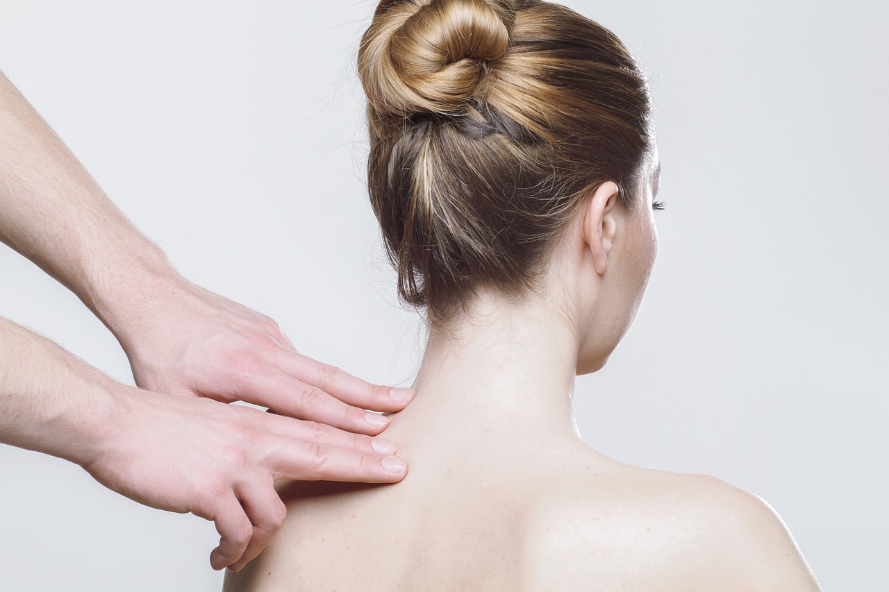 Therapeut drückt bei einer weiblichen Patientin Triggerpunkte im Nackenbereich.