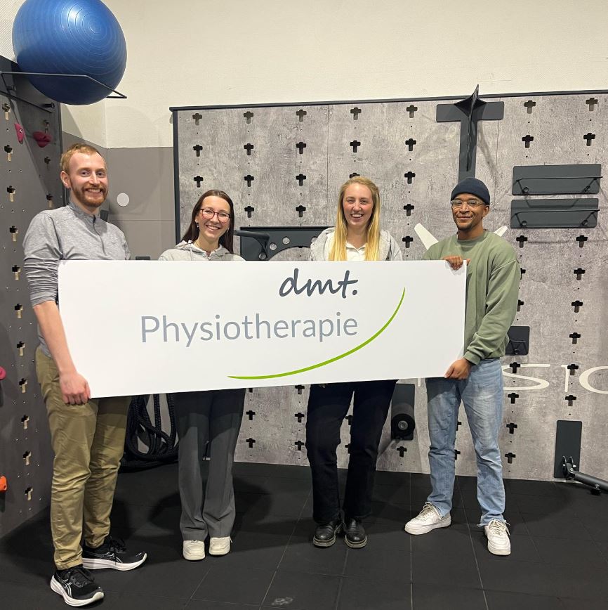 Auf dem Bild sieht man die Schildübergabe von Steffi und Celiné an die Mitglieder des Fördervereins Physiofreunde e. V.. Auf dem Schild ist in groß das Logo der dmt. Physiotherapie.