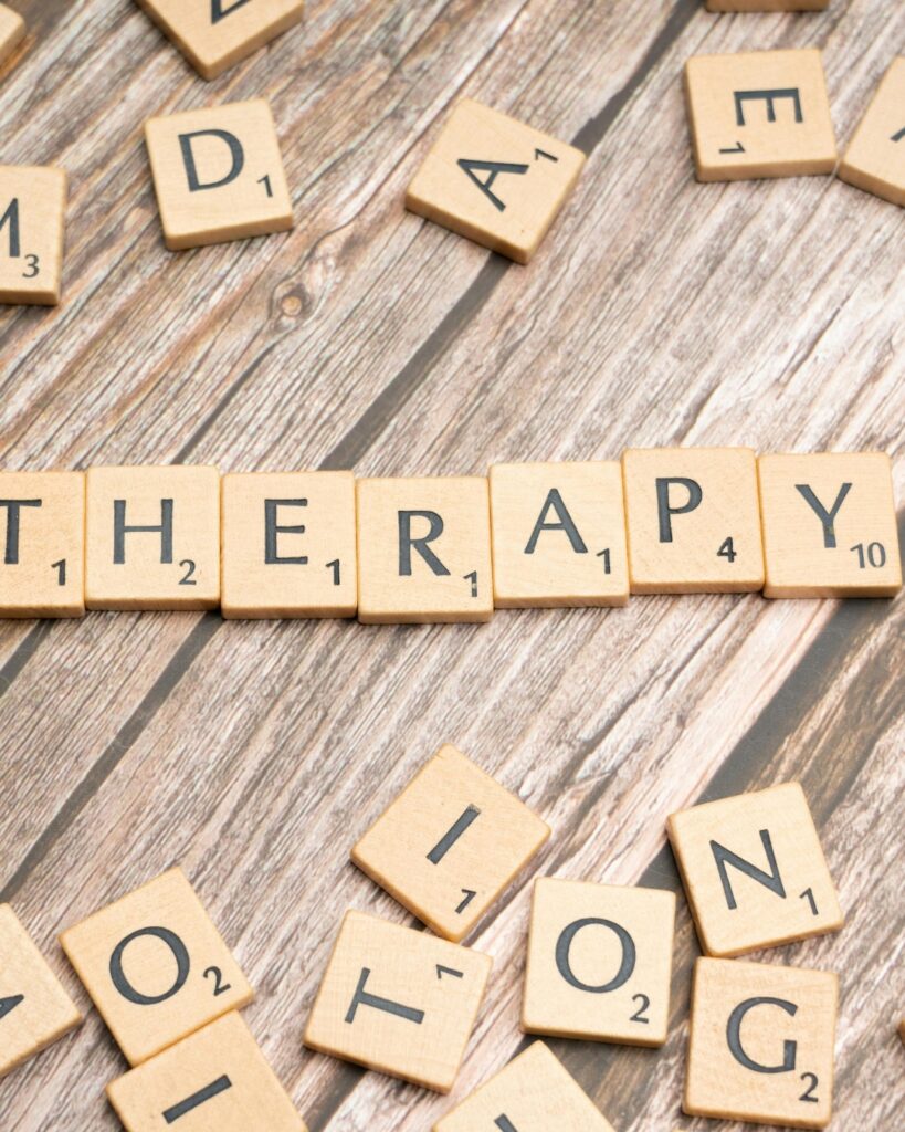Das Bild zeigt Holzplättchen mit Buchstaben. Die Buchstaben ergeben das Wort "Therapie".