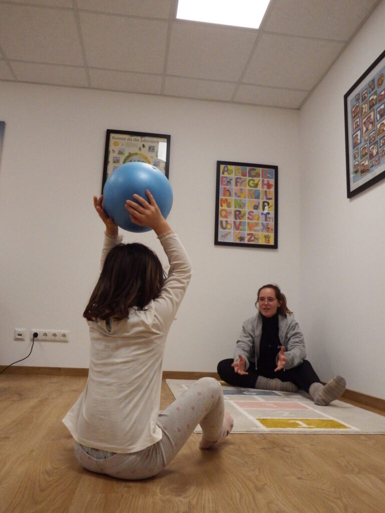 Jessi übt beim hin-und herrollen eines Balles mit ihrer Patienten das Sprechen.