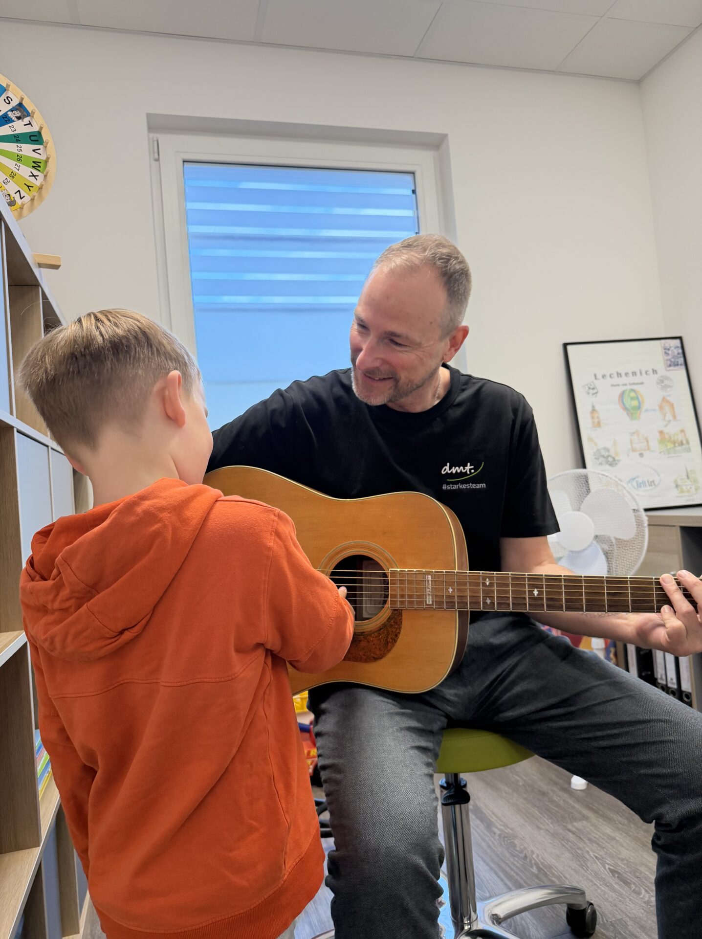 Thomas Logopäde der dmt. Therapie+ in Erftstadt spielt Gitarre und singt gemeinsam mit seinem jungen Patienten.