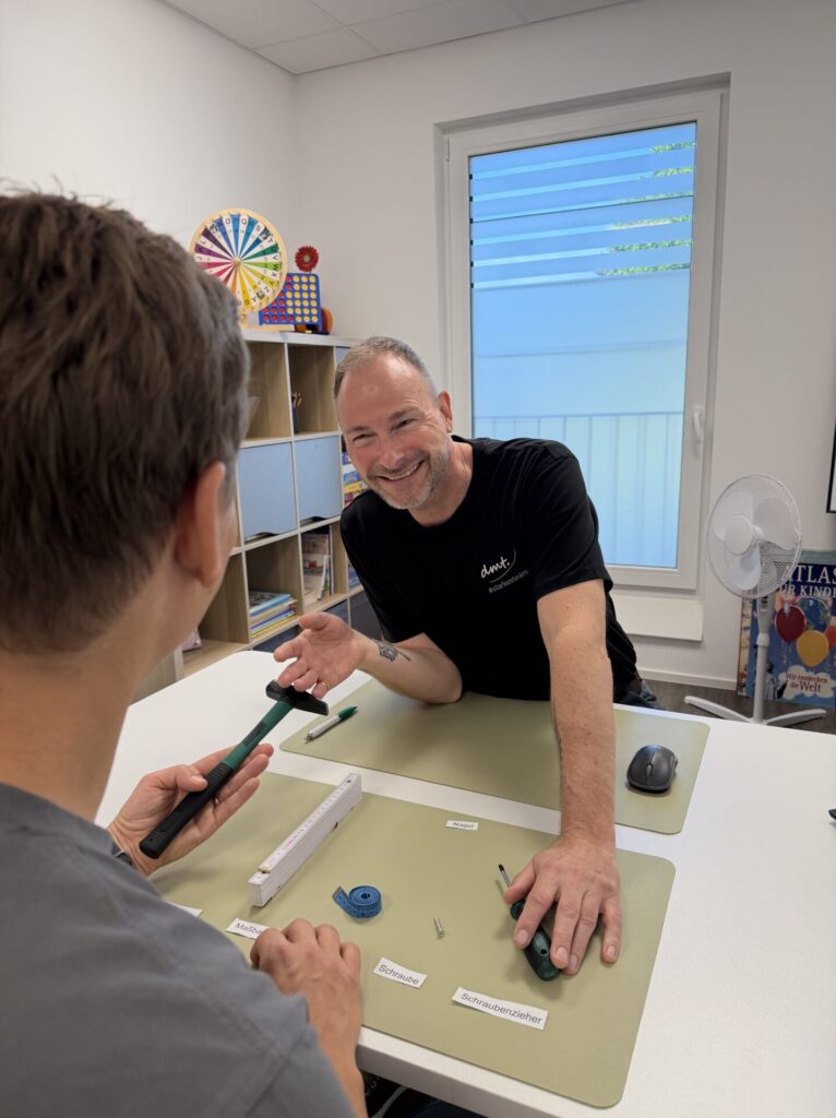 Thomas, Logopäde bei der dmt. Therapie+ in Erftstadt übt mit einem erwachsenen Patienten Gegenstände zu benennen.