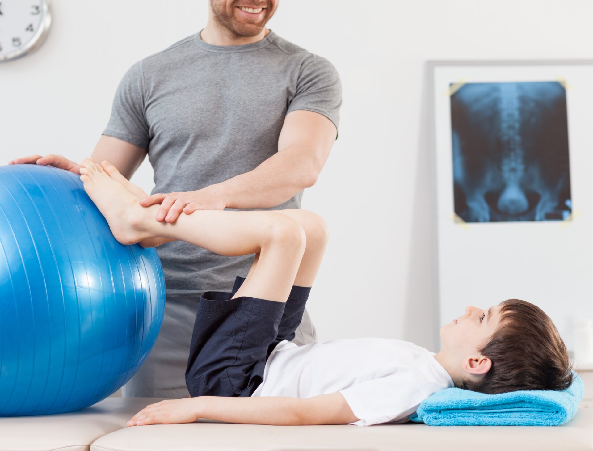 Kind liegt auf dem Rücken. Die Füße sind an einen Gymnastikball gestützt. Der Therapeut hält die Spunggelenke des Kindes sanft fest.